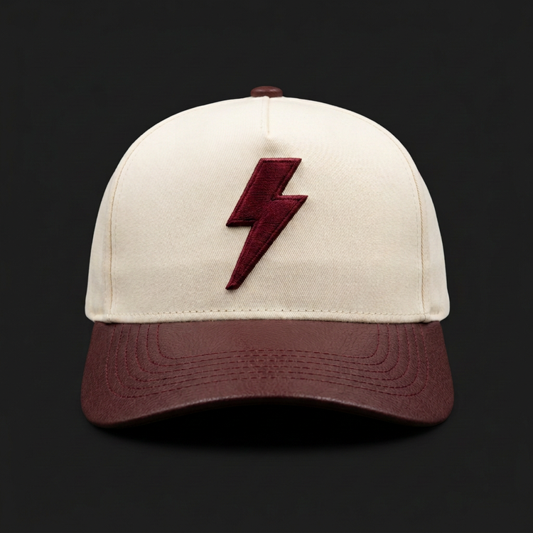Cream twill Saint Gabriel cap with raised oxblood lightning bolt and oxblood leather brim, front view
